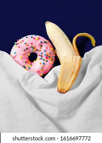 Banana and donut lie in bed under the covers. Sweet couple.