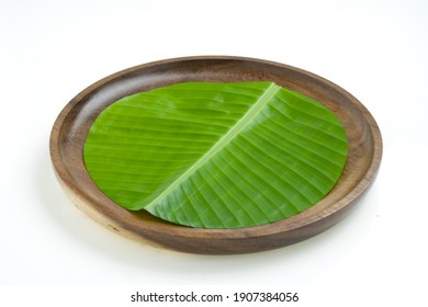Banana leaf,fresh green banana leaf  cut in circular shape and placed on a wooden plate with white  textured background ,isolated.
