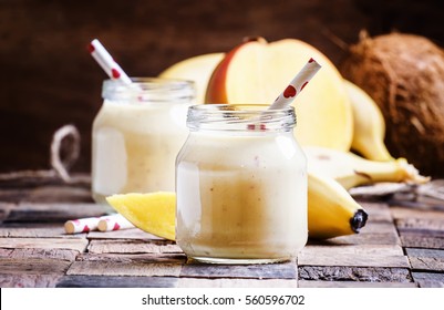 Banana mango smoothie with coconut in a glass jar, vintage wooden background, selective focus - Powered by Shutterstock