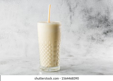 Banana Oats Smoothie Or Vanilla Milkshake In Glass On Bright Marble Background. Overhead View, Copy Space. Advertising For Milkshake Cafe Menu. Horizontal Photo.