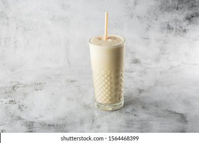 Banana Oats Smoothie Or Vanilla Milkshake In Glass On Bright Marble Background. Overhead View, Copy Space. Advertising For Milkshake Cafe Menu. Horizontal Photo.