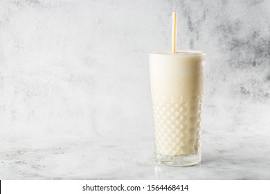 Banana Oats Smoothie Or Vanilla Milkshake In Glass On Bright Marble Background. Overhead View, Copy Space. Advertising For Milkshake Cafe Menu. Horizontal Photo.