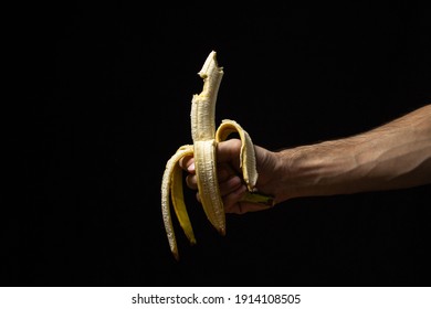 Banana on a black background. Healthy food. Male hand holding a peeled bitten banana on a black background