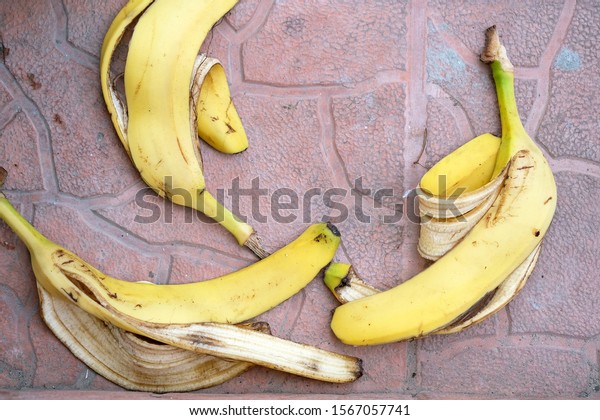 Banana peel on a red paving slab top view.\
Yellow banana peel thrown to the\
ground.
