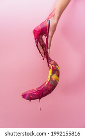 Banana in pink paint in hand. The paint flows down the banana. Creative photo for different topics.