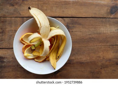 Banana Skin And Orange Peels In White Bowl On Wooden Table Background. Using Banana And Orange Peel In Compost Or Homemade Fertilizer. Zero Waste, Sustainable Living Concept. Top View, Copy Space