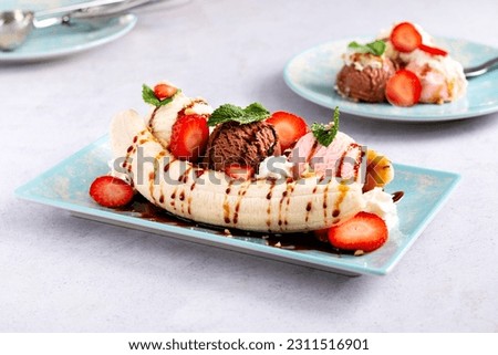 Banana split ice cream with syrup and strawberry on blue plate, top view