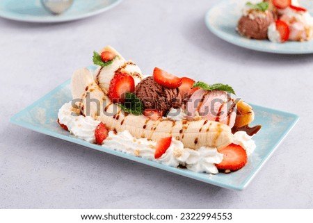Banana split ice cream with syrup and strawberry on blue plate, top view. Chocolate, strawberry and vanilla ice cream scoops on plate, summer dessert