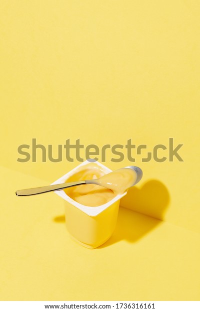 Banana and\
vanilla pudding or yogurt plastic cup on pastel yellow\
background.Minimal abstract food\
concept