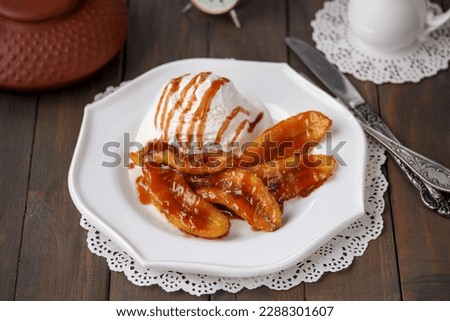 Bananas Flambe or Bananas Foster. A portion of sweet caramelized sliced bananas and a flambéed rum sauce served with scoop of vanilla ice cream on white plate. Selective focus, horizontal