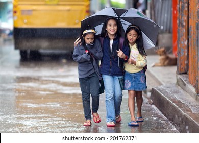 BANAUE, PHILIPPINES, DECEMBER 03 : Little girls are walking under the rain sheltering with an umbrella in the street of Banaue village, north Luzon, Philippines, on december 03, 2013