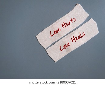 Band Aid Plaster On Gray Background With Handwritten Text LOVE HURTS LOVE HEALS, Concept Of Healing A Broken Heart, Fix A Wounded Painful Heartbreak