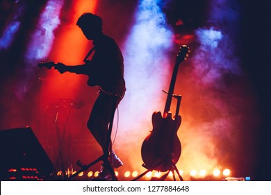 Band Silhouette. View Of Stage During Rock Concert With Musical Instruments And Scene Stage Lights, Rock Show Performance. Guitarist Plays Solo On Stage. Electric Guitar.