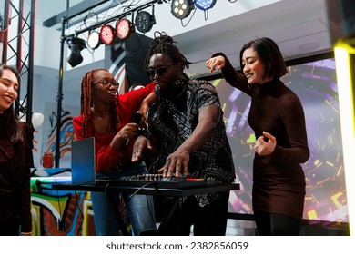 Band using dj station and dancing on stage at disco gathering in nightclub. African american frontman playing whille diverse women moving and engaging crowd to party at live concert - Powered by Shutterstock