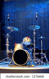 A Band's Percussion Kit Standing Empty Against A Background Of Blue Falling Water And Rocks. Space For Text On The Drum, Or On The Background.