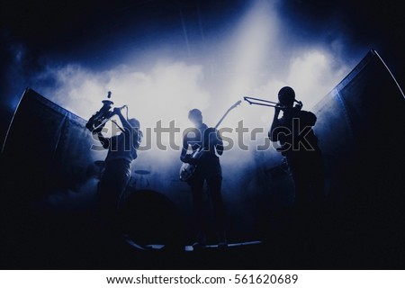Bands silhouettes with on a concert.  Group of saxophone, guitar, trombone players performing on stage.