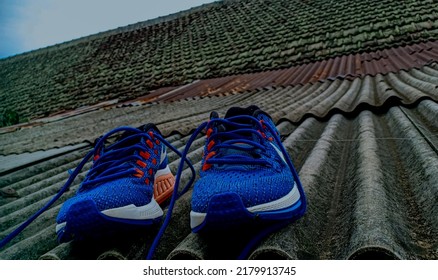 Bandung,  Indonesia, July 17, 2022 : Drying Blue Sports Shoes To Dry After Washing, With An Asbestos Tile Roof In The Background Of A House.