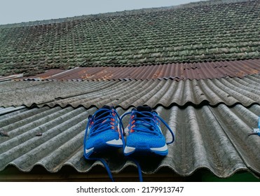 Bandung,  Indonesia, July 17, 2022 : Drying Blue Sports Shoes To Dry After Washing, With An Asbestos Tile Roof In The Background Of A House.