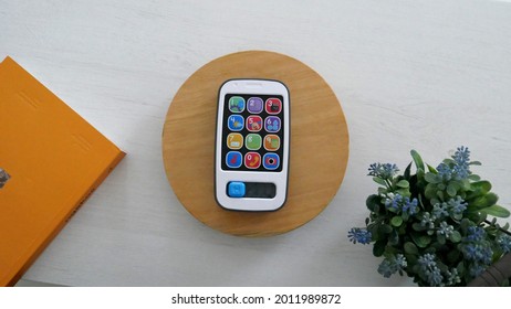 Bandung, Indonesia - March 03rd, 2021: Fisher Price Smart Phone Toy For Kid On The Round Wooden Tray And Plants