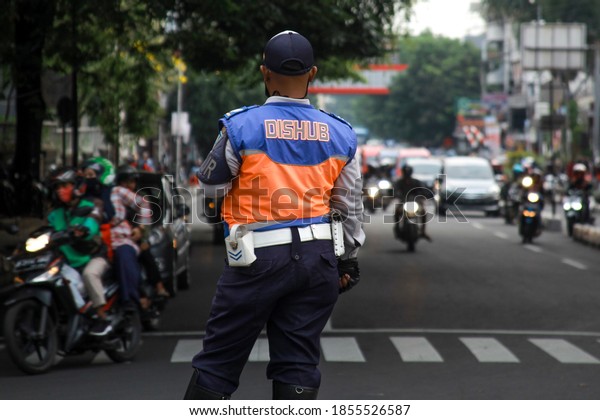 BANDUNG, INDONESIA - OCTOBER 2020: Traffic\
officer on duty from Department of Transportation. Transportation\
Agency (DISHUB) officer were standing in the middle of the road to\
regulate road traffic