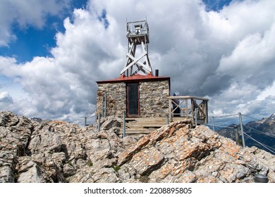 Banff, AB, Canada-August 2022; Low Angle Close Up View Of The Cosmic Ray Station And National Historic Site On Top Of Sulphur Mountain Against A White Clouded Blue Sky