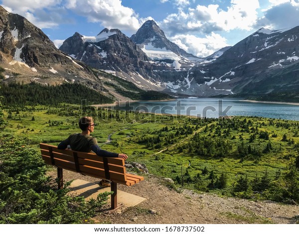 Banff, Alberta /\
Canada - July 30 2018: Man sitting on the bench with perfect view,\
Mount Assiniboine Provincial park at Alberta, Canada. (British\
Columbia, Relax, Meditation)\
