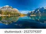 Banff National Park Lake Minnewanka autumn landscape. Alberta, Canada. Majestic mountains, forests in yellow green color against blue sky reflected on the water. Beautiful natural scenery.