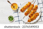 Bang Bang Chicken Skewers on white plate on white wooden table with bang bang sauce, chives, horizontal view from above, flat lay, free space