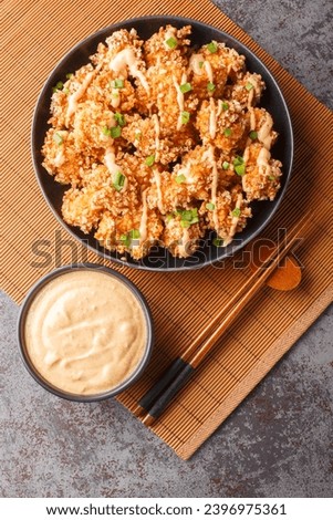 Bang bang chicken is a tender chunks of chicken coated in a crunchy Panko crust, fried to golden and finally smothered in a creamy, sweet and spicy sauce closeup. Vertical top view from above
