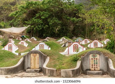 Bang Phra, Thailand - March 16, 2019: Chao Pho Khao Chalak Chinese Cemetery. Group Of Family Graves With Beige Tombstone With Colored Mandarin Letters Set Against Wall. Beige Shade Tarp Overhead.