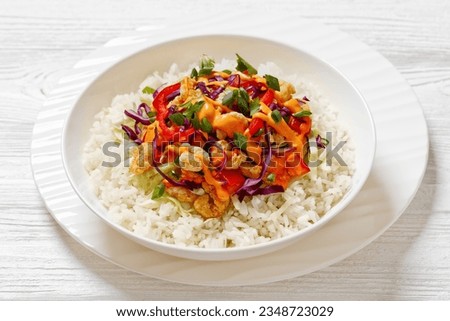 bang bang shrimp rice bowl with fried shrimps, shredded red cabbage, tomatoes, sweet red pepper and green onions topped with bang bang sauce on wooden table, horizontal view from above, close-up