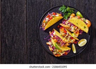Bang Bang Shrimp Tacos with purple coleslaw, tomatoes, parsley, lime and mayonnaise hot chili sauce on black plate on dark wooden table, horizontal view from above, flat lay, free space
