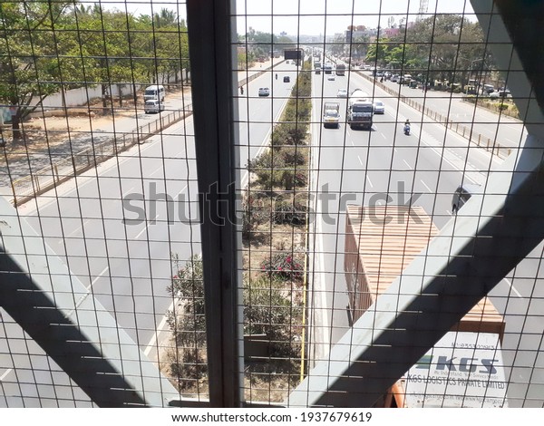 Bangalore, India - March, 17, 2021: Image of\
automobiles traveling under a overhead pedestrian bridge, looking\
down at the vehicles\
traveling.