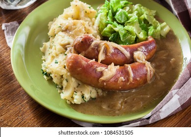 Bangers And Mash. Baked Sausage In Onion Gravy Served With Mashed Potatoes And Cabbage