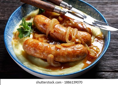 Bangers and mash traditional british dish of pork sausage with onion gravy and mashed potato on a blue plate with cutlery on a dark wooden background, top view, close-up