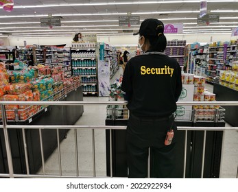 Bangkok Thailand 08-10.2021 Back Of Asian Female Security Staff Wearing Cap And Face Mask Standing Behind A Steel Barricade Observe Customers Who Do Not Wear A Mask During Shopping In Supermarket.