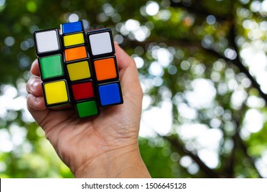 Bangkok, Thailand, 14 September 2019, Woman's Hand Holding Rubik's Cube And Playing With It, In Bokeh Green Background, Rubik's Cube Invented By A Hungarian Architect Erno Rubik In 1974, Game Concept