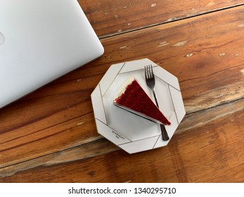 Bangkok, Thailand; 17 February 2019: Top View Red Velvet Cheesecake  With The White Dish And Laptop On A Wooden Table. The Cafe Coffee And Homemade Bakery.