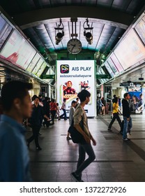 BANGKOK , THAILAND - APRIL 14 , 2019. People Passing By In BTS Siam Station For Transition To Another Train Line With Billboard Behind Them.