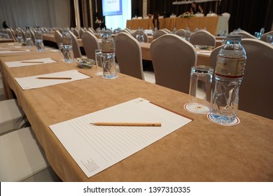 BANGKOK, THAILAND - APRIL 2, 2018: Pencil On Paper Note With Bottle Of Water, Glasses And Coaster Set Up Classroom Style With Oblong Table Cloth For Annual General Meeting In Hotel Ballroom. 