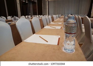 BANGKOK, THAILAND - APRIL 2, 2018: Pencil On Paper Note With Bottle Of Water, Glasses And Coaster Set Up Classroom Style With Oblong Table Cloth For Annual General Meeting In Hotel Ballroom. 