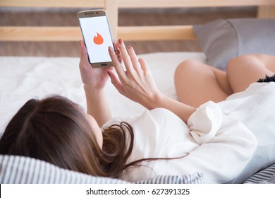 BANGKOK, THAILAND APRIL - 25 2017: woman lying down on the bed while using her mobile phone log in to the application Tinder in her bedroom