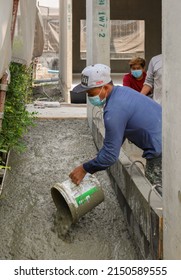 BANGKOK, THAILAND - APRIL 9, 2022 :   Thai Worker Pouring Wet Cement From A Bucket On Wheelchair Ramp Floor At Home Construction Site