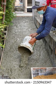 BANGKOK, THAILAND - APRIL 9, 2022 :   Thai Worker Pouring Wet Cement From A Bucket On Wheelchair Ramp Floor At Home Construction Site