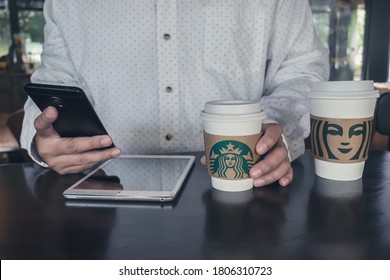 BANGKOK, THAILAND - August 31, 2020:  Businessman Working On Apple IPad And Smarthphone In The Starbucks Coffee Shop With A Starbucks Paper Cup Of Espresso. Illustrative Editorial 