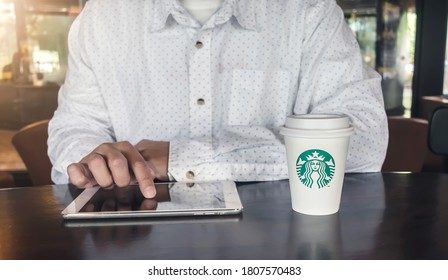 BANGKOK, THAILAND - August 31, 2020:  Businessman Working On Apple IPad In The Starbucks Coffee Shop With A Starbucks Paper Cup Of Espresso. Illustrative Editorial 