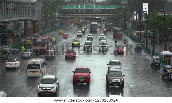 BANGKOK,  THAILAND - CIRCA
OCTOBER 2018 : View of STREET TRAFFIC near CHIT LOM train station
in HEAVY RAIN.  Many CAR, BUS, TAXI, MOTORBIKE and TUK TUK on the
road.