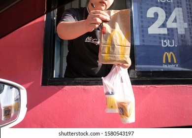Bangkok, Thailand - Dec 5, 2019: McDonalds worker handing brown paper bag of fast food and coffee cups through window of car drive thru service, McDonald's is an American fast food restaurant chain