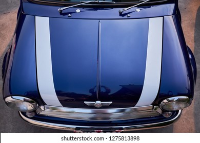 
BANGKOK, THAILAND - December 22, 2018: Vintage Mini Cooper Car Top View Of Shiny Hood & Logo On Bonnet. Reflection On Blue Paint And White Stripe. The Austin Mini Is Vintage Small Economy Car.