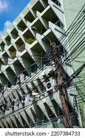 Bangkok, Thailand - February 13, 2022: Busy And Intertwined Electric Wires In Front Of Green Building With Pattern Sunshade.